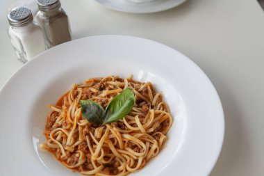 Yeşil yapraklarla süslenmiş yuvarlak bir tabakta iştah açıcı spagetti.
