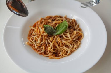 Yeşil yapraklarla süslenmiş yuvarlak bir tabakta iştah açıcı spagetti.