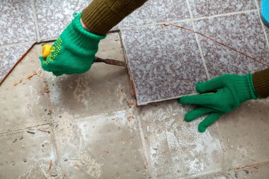 Fayansların sökülmesi. Yeşil eldivenli eller, kırık fayansı keskiyle baltalıyor.