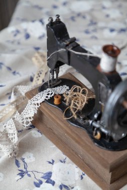 Klasik el yapımı dikiş makinesi ve beyaz kumaş arka planında mavi desenli bir iplik yumağı.