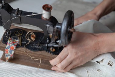 Beyaz iplik makarası olan klasik dikiş makinesi beyaz bir kumaşın üzerinde duruyor. Dişinin elinde pıhtı var.