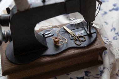 Hayat dikiyorum. Sarı antika makas elle dikilen bir dikiş makinesinin yatağında yatıyor. Yakınlarda ahşap bir makara var.