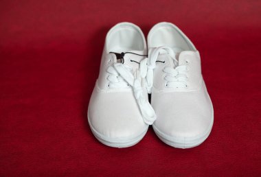 Bağcıklı iki yeni beyaz spor ayakkabı kırmızı izole bir arka planda duruyor.