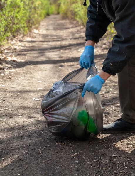我们把大自然从垃圾中拯救出来 身穿蓝色橡胶手套的生态学家在泡沫中的黑色塑料袋中收集垃圾 — 图库照片