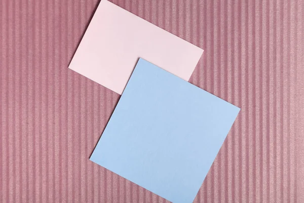 An interesting play of colors and textures. Two smooth sheets of pink and blue paper lie on brown paper with vertical stripes. Place for inscriptio