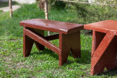 Küçük kahverengi ahşap bank yeşil çimlerin üzerinde duruyor. Yakınlarda daha büyük bir bank var.