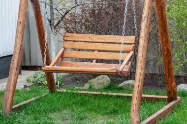 Şirin kahverengi ahşap salıncak, çayırdaki yeşil çimlerin üzerine monte edilmiş ahşap direklerde sallanıyor.