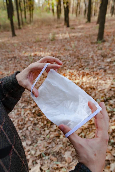 Viral safety in the forest. Hands hold a white medical mask in front of them in the spring forest. Close-u