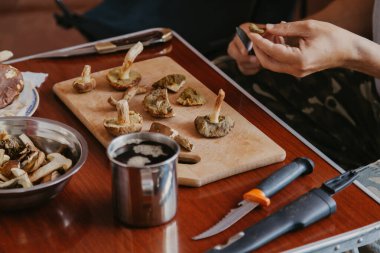 Toplanan mantarların incelenmesi. Tahta bir yaban domuzunun üstünde yenebilir mantar kesen bir adamın elleri.