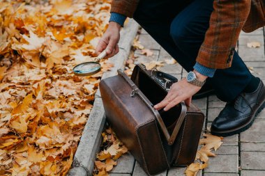 Kareli ceketli bir adam bir sonbahar parkının arka sokağındaki kahverengi bir halı çantasından büyüteç çıkardı. Yukarıdan Görünüm