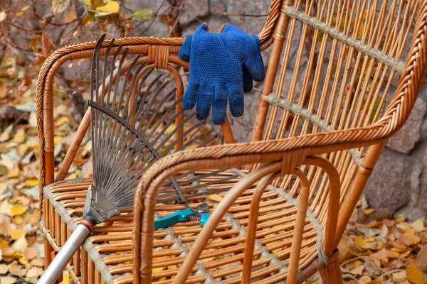 秋天的平静生活 秋天的公园里 一把扇子耙和一把花园剪子躺在一把漂亮的柳条椅子上 旁边是蓝色手套 Close — 图库照片