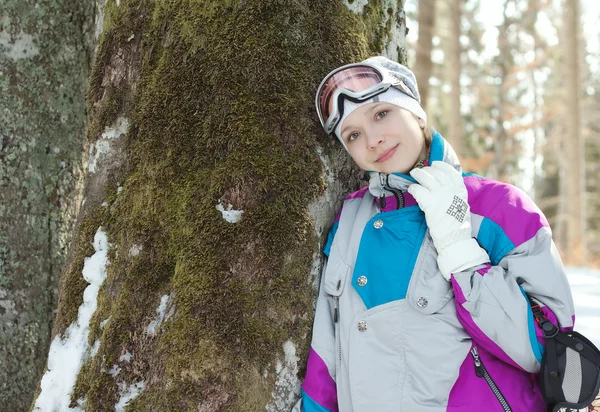 Mujer esquiadora de pie cerca del tronco de un árbol en el bosque de invierno —  Fotos de Stock