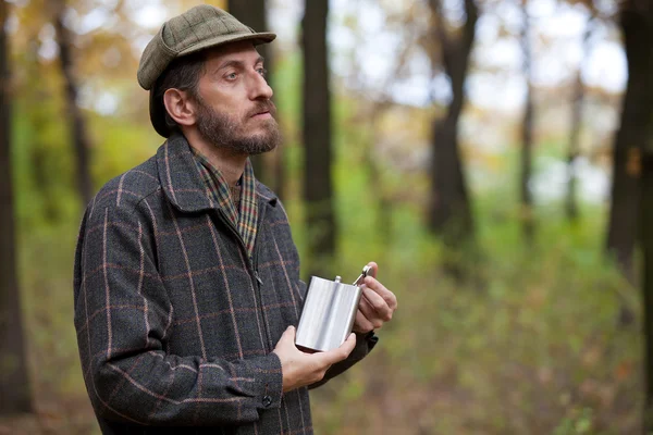 Man with beard opens the flask in autumn forest — Stock Photo, Image