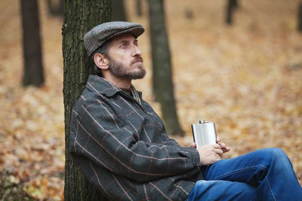 Man with a beard sitting in the autumn forest with a flask in hi — Stock Photo, Image