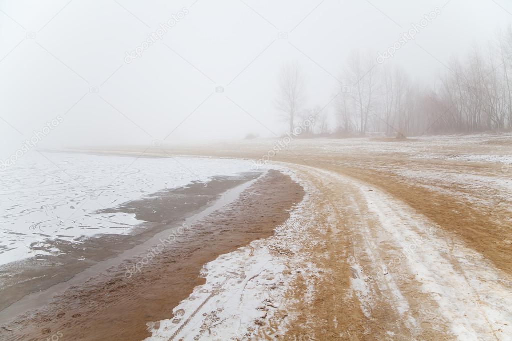 Sandy beach by the river in the fog in winter