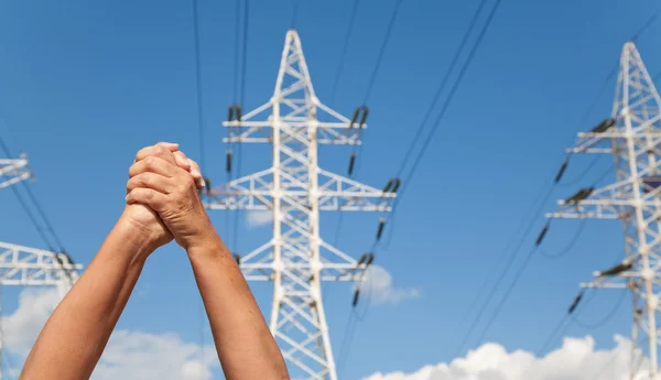 Hands crossed in assent and power transmission lines against blu