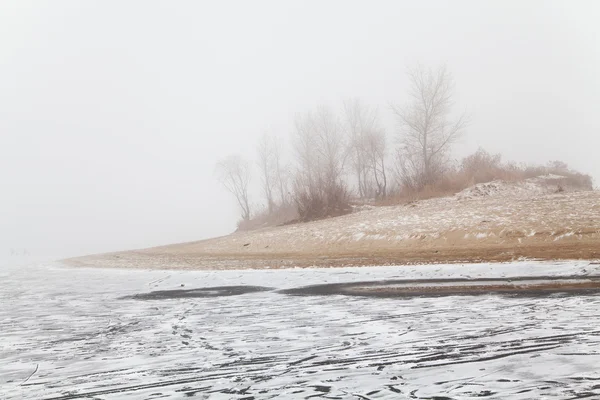 Hill in the fog on a winter frozen river beach — Stock Photo, Image