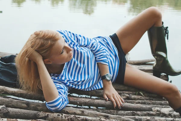 Beautiful blonde woman lying on old fishing bridge — Stock Photo, Image