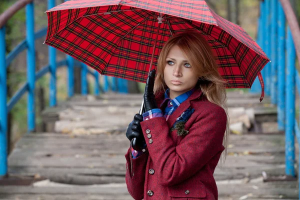 Beautiful blonde woman stands on bridge under umbrella — Stock Photo, Image