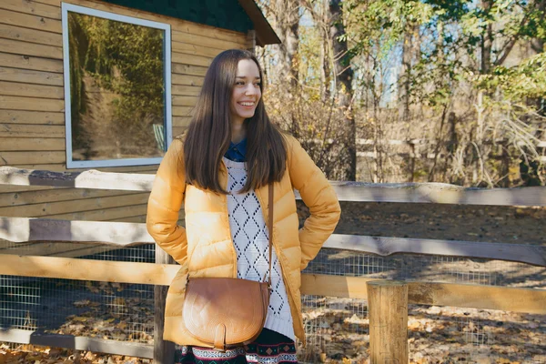 Young beautiful girl stands near the wooden fence in city zoo — Stock Photo, Image