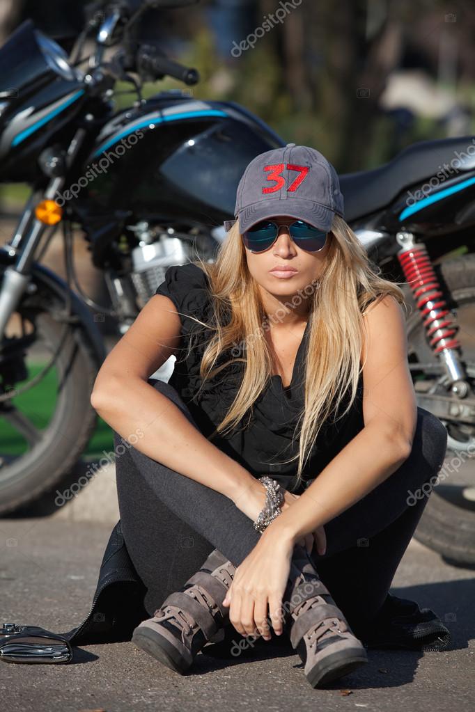 Young biker girl sitting in front of a motorcycle — Stock Photo