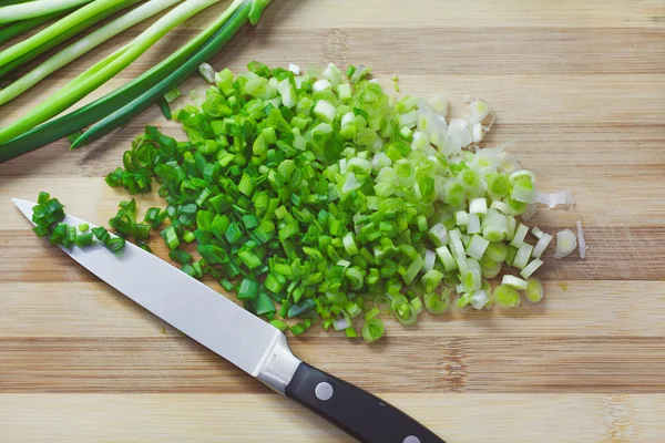 Handful of chopped green onions on striped wooden board — Stock Photo, Image