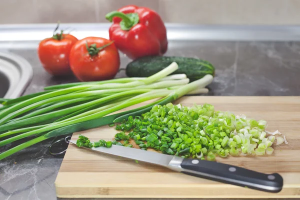 Cebolas e legumes verdes picados em tábua de madeira listrada — Fotografia de Stock