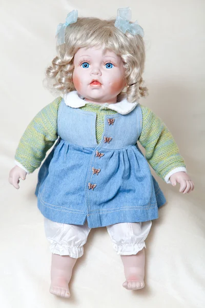 Muñeca niña de ojos azules sentada sobre fondo de luz suave — Foto de Stock