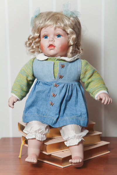 Vintage porcelain doll blonde sitting on stack of books