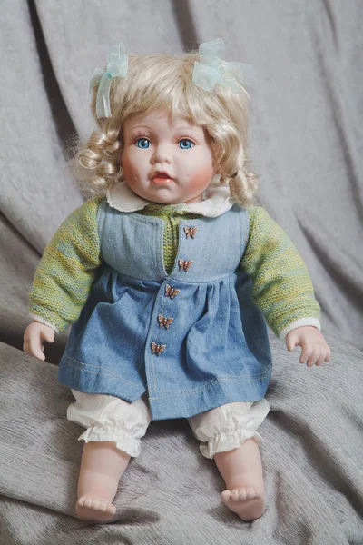 Muñeca de porcelana vintage rubia sobre fondo de tela gris — Foto de Stock