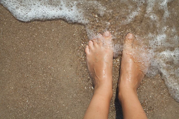 Barefoot female feet in foam of sea