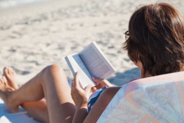 Yaşlı kadın plajda kitap okuma