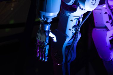 Pembe ışıktaki robot vücudu koyu bir arka plana karşı. Birkaç parmağı olan mekanik bir el açıkça görülebilir.