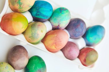 Paskalya tatiline özen göster. Farklı renklerde boyanmış birkaç tavuk yumurtası hücreli plastik bir kapta bulunur. Yakınlarda üç yumurta var.