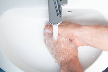 A man washes his hands over a white tiled sink. A stream of water pours from a chrome faucet close-up. View from abov
