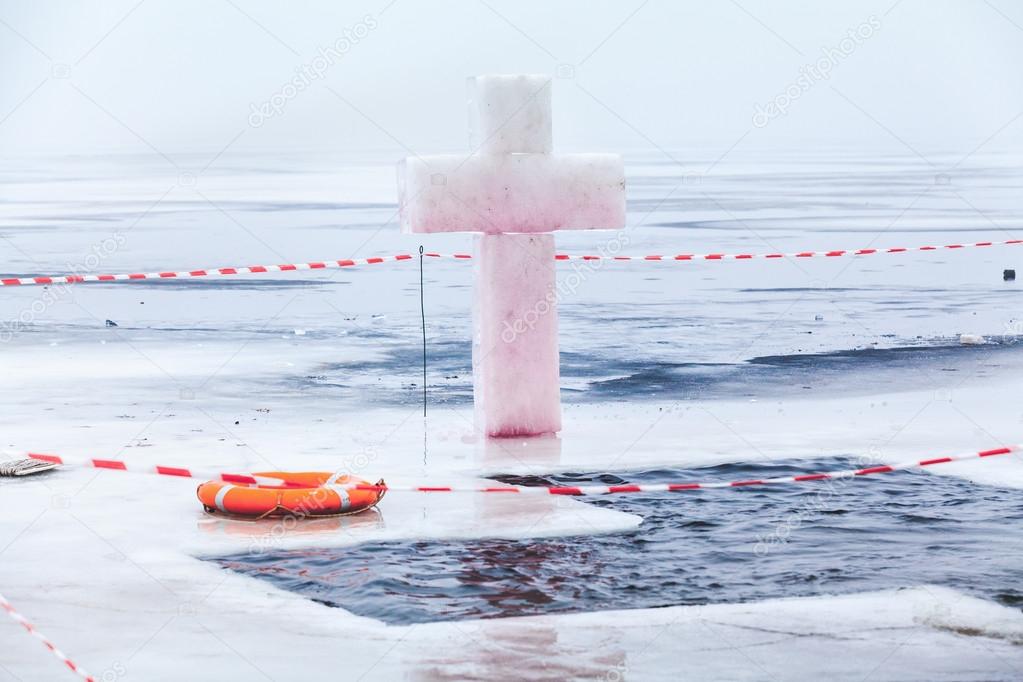 Ice cross and hole in winter pond on Epiphany