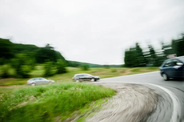 Três carros dirigindo em uma curva em uma estrada de estrada do país — Fotografia de Stock