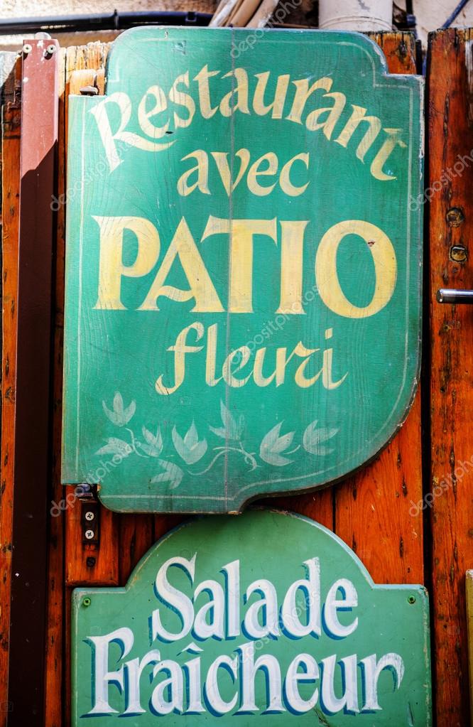 Vintage restaurant name painted on green wooden plaque showing Restaurant avec Patio Fleuri translated as Restaurant with Patio in bloom