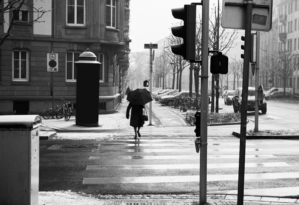 Old woman with umbrella crossing street — Stockfoto