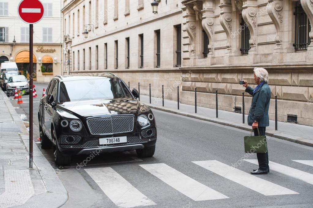 PARIS, FRANCE - MAY 21, 2016: Man taking photo of the luxury Bentley Bentayga Hybrid SUV on the streets of Paris, France
