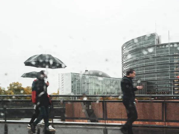 Pedoni che camminano con gli ombrelloni davanti al Parlamento europeo — Foto Stock