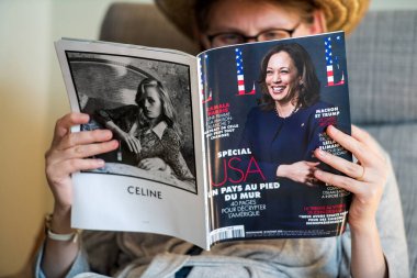 Woman reading in living room the latest Elle Magazine featuring on cover Kamala Harris clipart