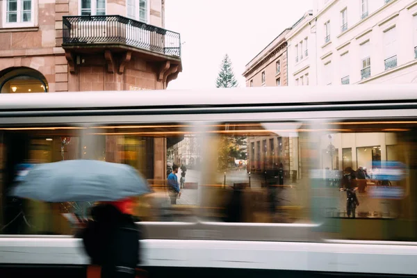 La silhouette delle persone con l'ombrello davanti al tram in movimento sulla strada quasi vuota — Foto Stock