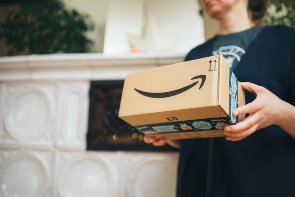 Seitenansicht einer eleganten Frau, die ein Amazon Prime-Paket mit einem pfeilgrinsenden Schriftzug und einem Luxus-Ofen im Hintergrund als Geschenk hält — Stockfoto