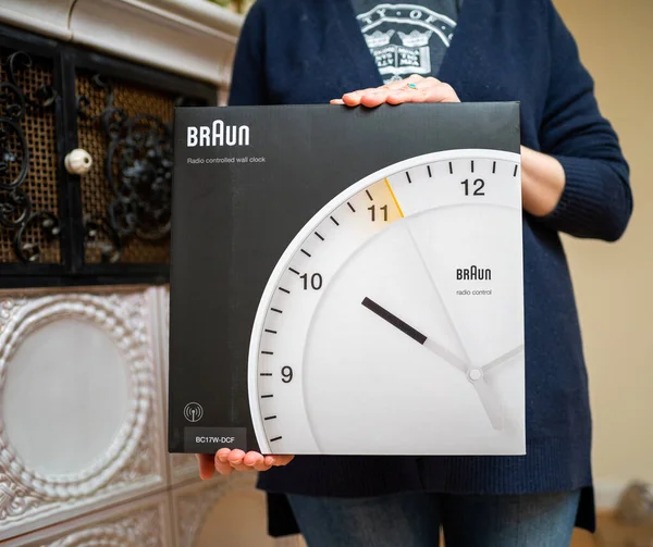 Mujer mostrando la presentación del nuevo reloj de pared controlado por radio Braun BC17W-DCF - paquete grande de la icónica firma de diseño alemana — Foto de Stock