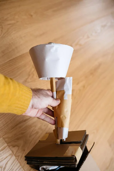Main masculine tenant neuf enveloppé dans une lampe de table en papier contre du bois — Photo