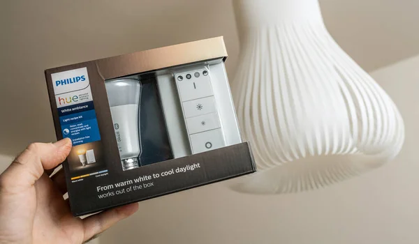 POV męska ręka trzymająca pakiet nowego Philips Sify HUE smart light for home z białą oprawą oświetleniową w tle — Zdjęcie stockowe