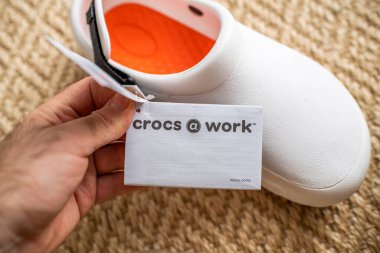 POV erkek, iş yerinde Crocs 'un reklam etiketini tutuyor. Fiyat etiketli rahat ayakkabılar.