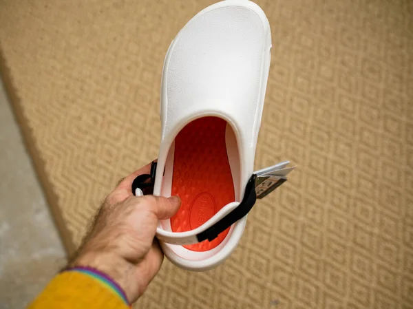 POV mano masculina sosteniendo contra fondo de alfombra Crocs en el trabajo zapatos cómodos —  Fotos de Stock