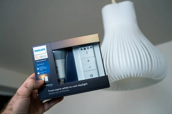 POV male hand holding the package of new Philips Signify HUE smart light for home with white light luminaire in background — Stock Photo, Image